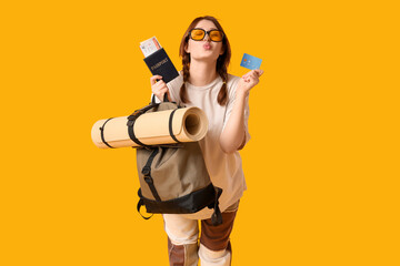 Smiling young woman with passport and credit card on yellow background. Travel concept