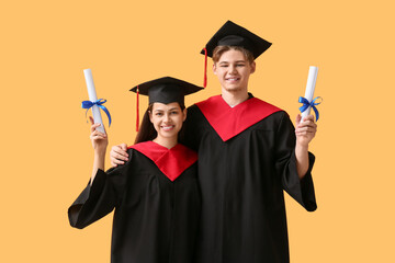 Happy graduate couple with diplomas on yellow background