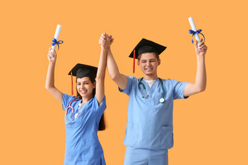 Happy medical graduate couple with diplomas on yellow background