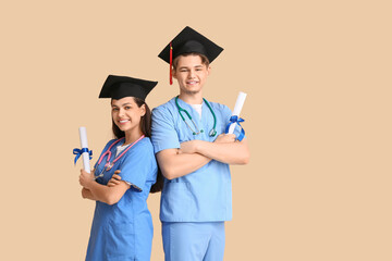 Happy medical graduate couple with diplomas and stethoscopes on beige background