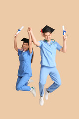 Happy medical graduate couple with diplomas and stethoscopes near beige wall