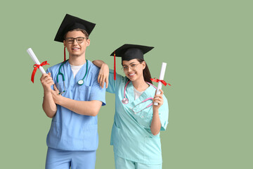 Happy medical graduate couple with diplomas and stethoscopes on green background