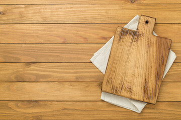 Cutting board with napkin on wooden background, top view