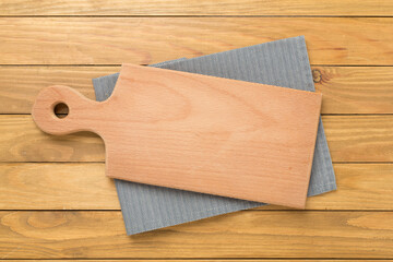 Cutting board with napkin on wooden background, top view