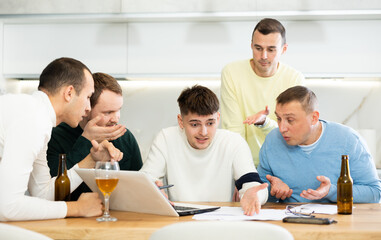 Fototapeta premium Group of male friends solving problems using laptop and drinking beer at home
