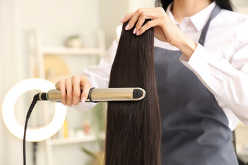 Naklejka premium Hairdresser straightening long dark hair with a flat iron, professional hair care and styling, beauty salon service