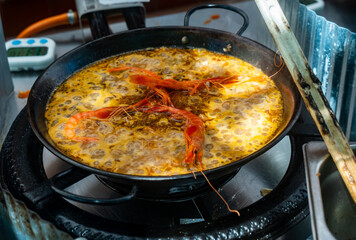 Sea paella is cooked on camping gas stove. Process of cooking seafood paella in large frying pan. Dish is supplemented with several tiger shrimps