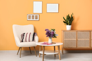 Interior of stylish living room with bouquet of lilacs branches on coffee table, magazine and cozy armchair