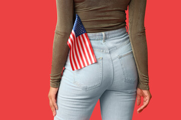 Beautiful young African-American woman with USA flag on red background, back view