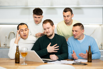 Fototapeta premium Group of joyful friends watching football match on a laptop together and drinking beer