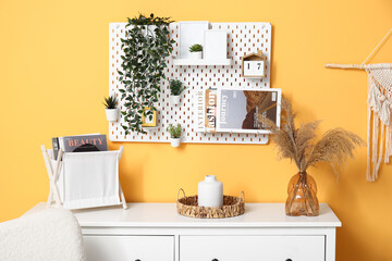 Vase with pampas grass on chest of drawers and pegboard on orange wall in living room