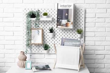 Pegboard with magazine, photo frame and houseplants on white brick wall in living room
