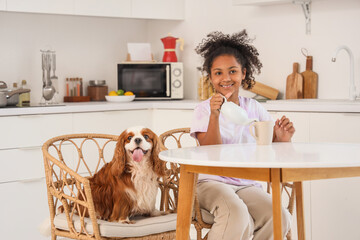 Teen African-American girl with teapot and cute cavalier King Charles spaniel sitting at table in...