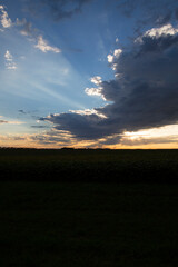Sunset Light Shining Through Large Diagonal Cloud Over Open Field and Colorful Horizon Blue Sky

