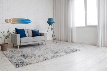 Interior of beautiful living room with cozy sofa, houseplant, surfboard and carpet