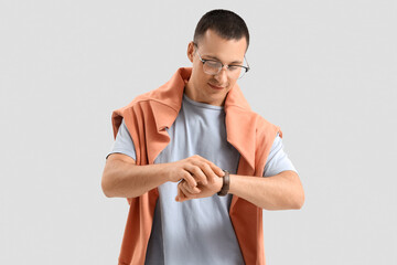 Handsome young man in stylish outfit looking at wristwatch on grey background
