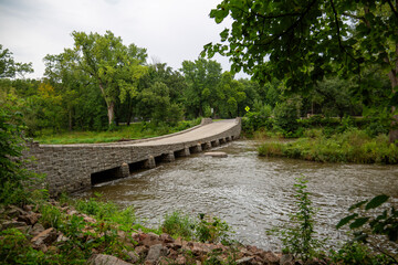 Fototapeta premium Unique Rock Bridge with Downward Dip Over a Beautiful River Surrounded by Trees – Scenic Nature and Architectural Design