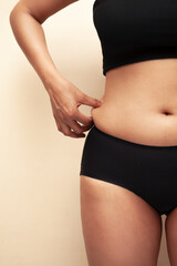 A woman squeezing his excessive belly fat on light yellow background, Healthy concept.