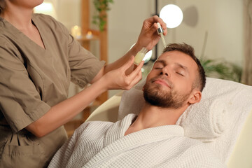 Fototapeta premium Handsome young man receiving facial massage with serum in beauty salon