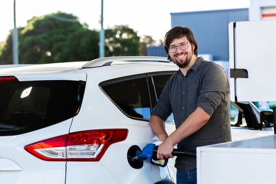 Happy young man in his twenties filling car with petrol at servo