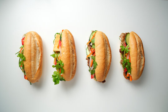 Top-down shot of four banh mi lined up on blank background
