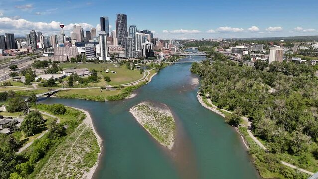 Cinematic aerial shot of the Bow River flowing past Downtown Calgary overlooking the East Village and pathways.
