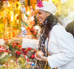 Confident Latin American woman who came to an open-air fair on the eve of the holidays chooses Christmas souvenirs and toys ..to buy them