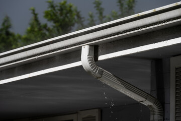 Dark stormy day, rain water overflowing roof gutter and clogged downspout, residential house...