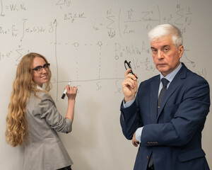 Female student answers a question from an elderly professor at a white board. 
