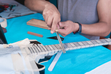 Black electric guitar in repair shop with the hands of a guitar luthier fixing it, frets alignment.