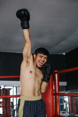 Potrait Of Asian Fighter Guy Winning The Match, Clenching Fist And Raised Hand In Boxing Ring