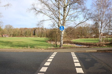A tranquil rural crosswalk in the countryside, lined by a bike path and green fields under the sky