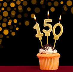 Number 150 birthday candle - Cupcake on black background with out of focus lights