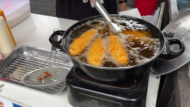A woman preparing and selling deep fried corn dog stuffed with cheese and sausage in oil. Street food concept.