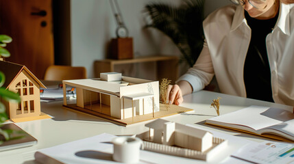 close-up of female architect showing 3D cardboard model of house project to a client in architecture design studio, professional meeting