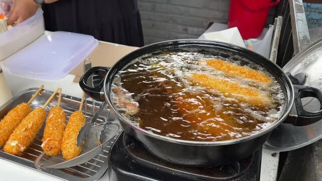 A woman preparing and selling deep fried corn dog stuffed with cheese and sausage in oil. Street food concept.