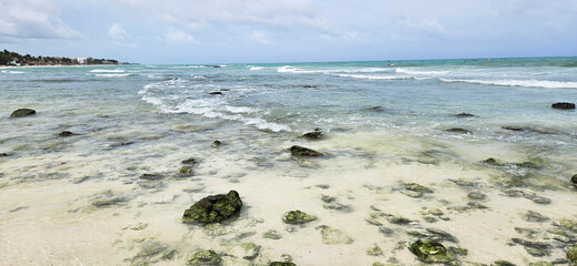 Fototapeta premium Beach and sea on a rainy day. Rocks covered in algae. Cloudy sky. Tides roll onto the beach. 