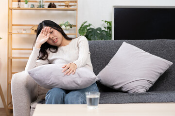 Obraz premium Young woman having a premenstrual headache on the sofa in a modern living room.