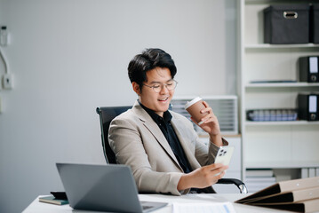 Fototapeta premium Confident Asian businessman typing laptop computer and digital tablet while holding coffee