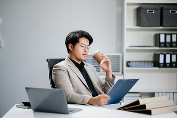 Fototapeta premium Confident Asian businessman typing laptop computer and digital tablet while holding coffee