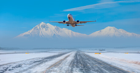 Passenger airplane fly up over take-off runway snowy mountains in the background - Snow-covered...