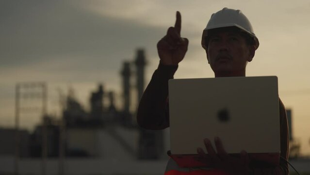A man wearing a hard hat and safety vest is pointing at a laptop. He is likely giving directions or instructions to someone else