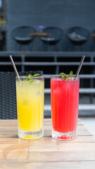 Colored summer lemonades in glasses with ice and mint on wooden table on cafe background