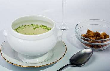 Ceramic soup tureen with consommé, accompanied by a plate of toasted bread.