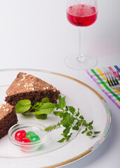 Plate with chocolate cake, garnished with green and red cherries and a sprig of mint.