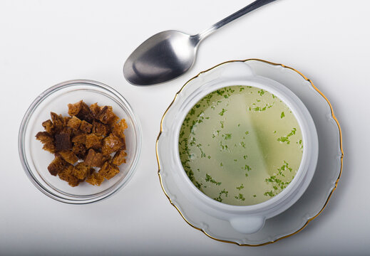 Ceramic soup tureen with consomm&eacute;, accompanied by a plate of toasted bread.