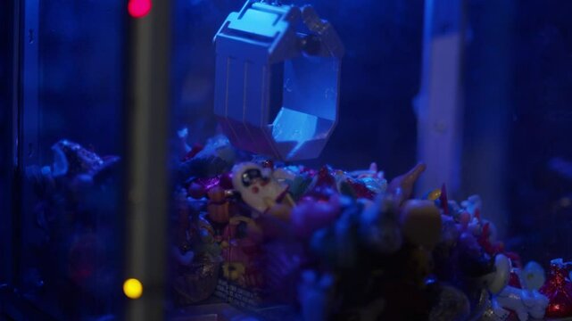 Claw crane arcade game with prize toys and candy available, in a close up shot with LED lights flashing.