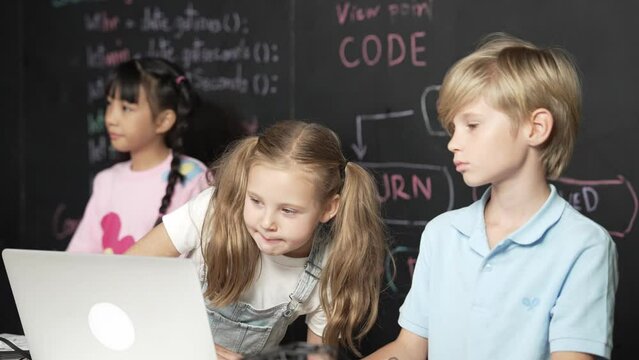 Smart girl using laptop programing engineering code with diverse friends ay table with microchip and main board scatter around in STEM classroom at blackboard written with coding prompt. Erudition.