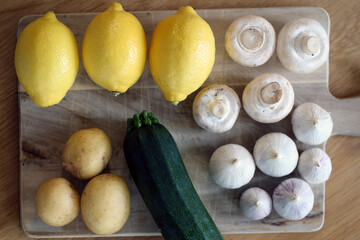 Scandinavian summer, fall season cuisine. Ingredients for a healthy meal: potatoes, garlic, zucchini and lemons on a wooden rustic cutting board. Fresh raw vegetables from season's harvest. Closeup.