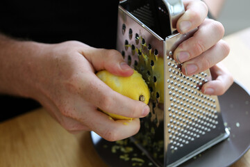 A white man grating lemon zest with a grater. Preparing food. Refreshing ingredients for cooking and baking. Closeup color image of the lemon, grater and the hand of the man. Healthy lifestyle image.